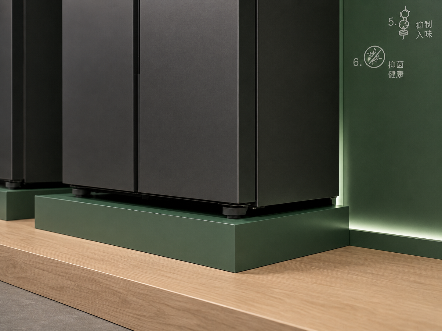 Close-up of closed graphite Bosch refrigerator on a dark-green base beside illuminated feature wall and light-oak platform