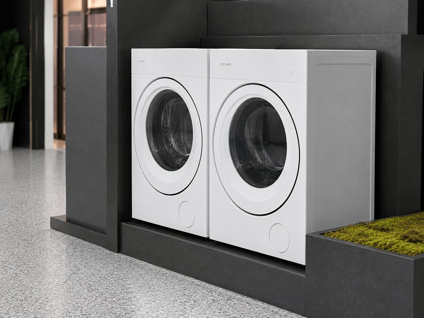 Close view of two white COLMO front-loading laundry appliances fitted into dark custom island display bays