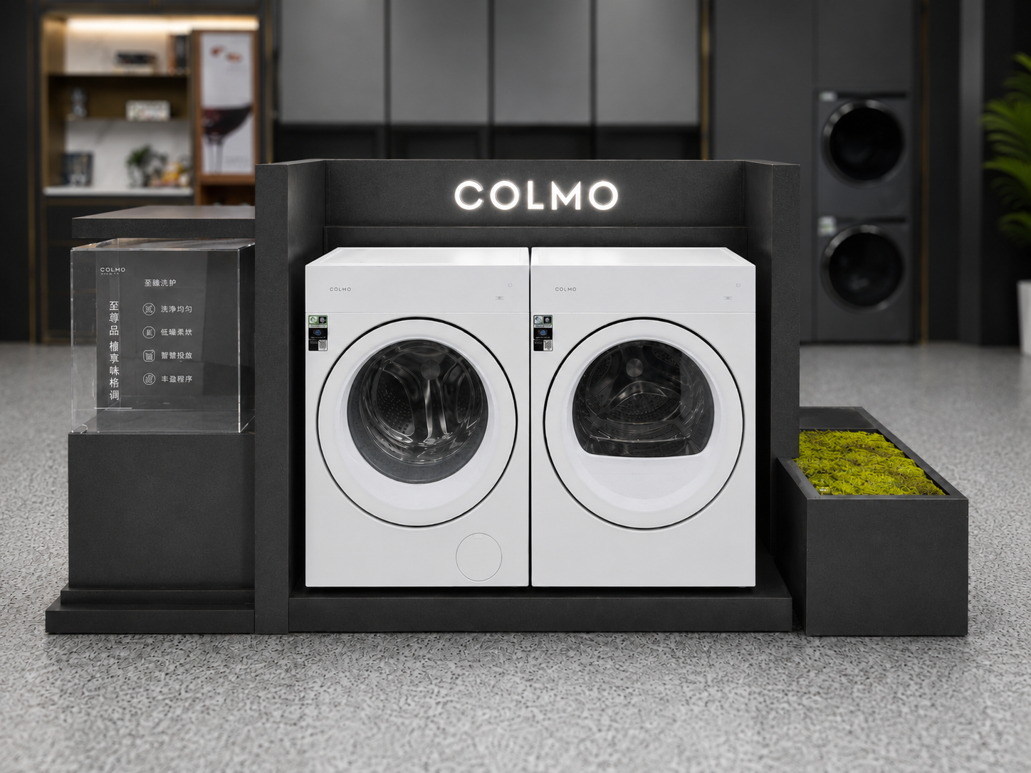 Front view of COLMO laundry appliance island display with two white front-loading appliances, illuminated COLMO sign, transparent information module and planting accent