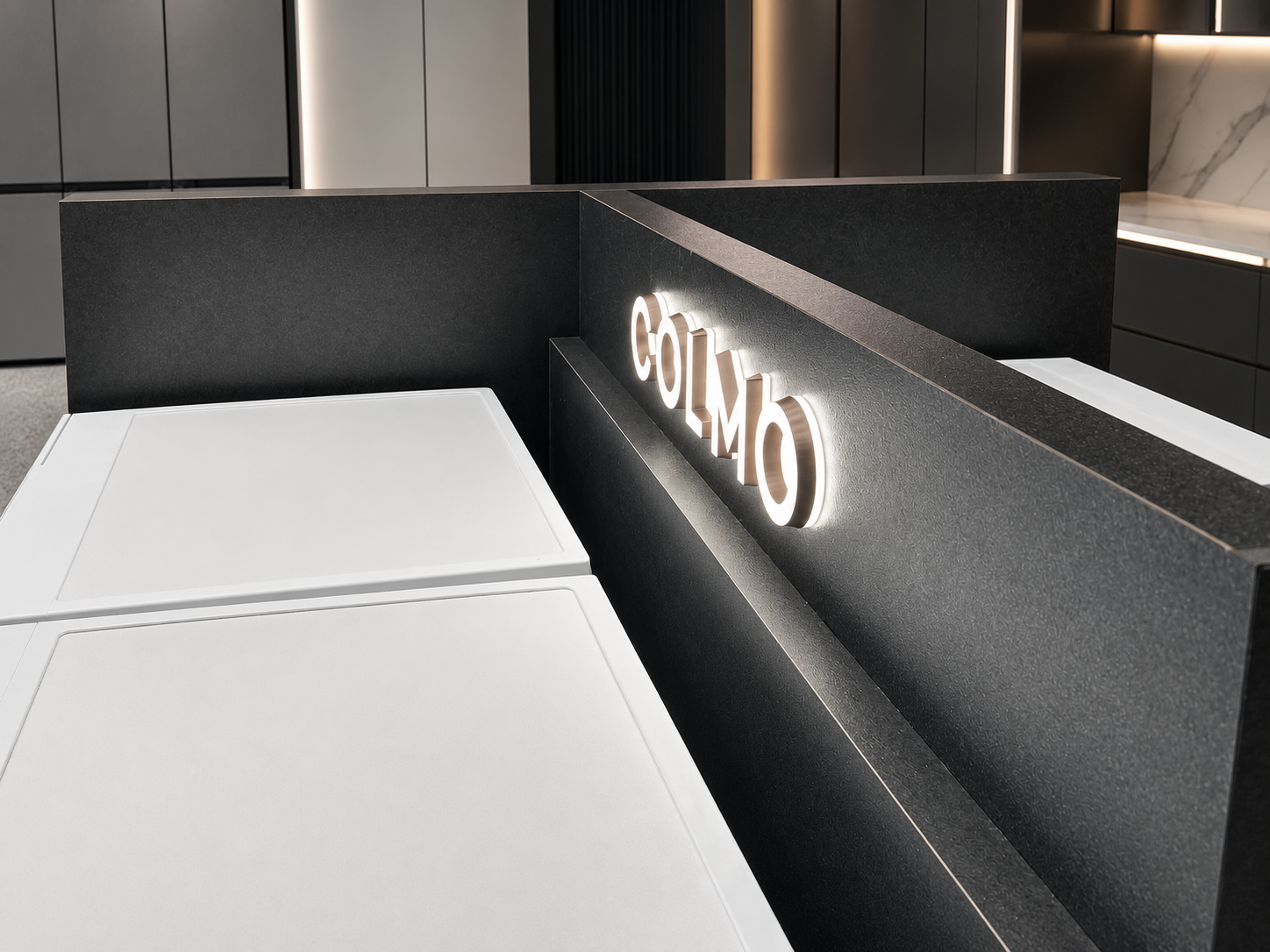 Angled close-up of illuminated COLMO lettering, dark textured structural panels and the refined top-surface finishing of the island display
