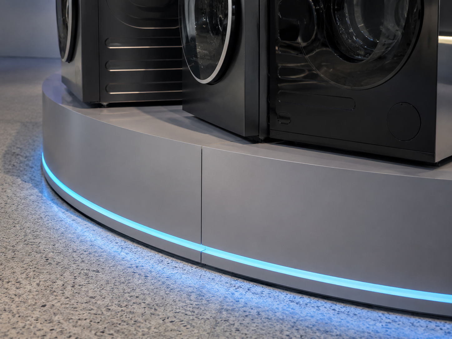 Close detail of curved grey platform panels, precise joints and continuous blue LED edge lighting beneath Little Swan washer display