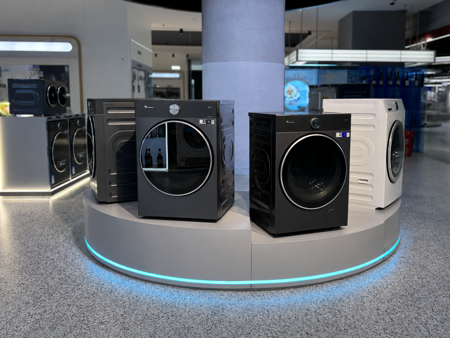 Front showroom view of Little Swan circular washer platform showing four appliance positions, central column, radial canopy and illuminated brand ring