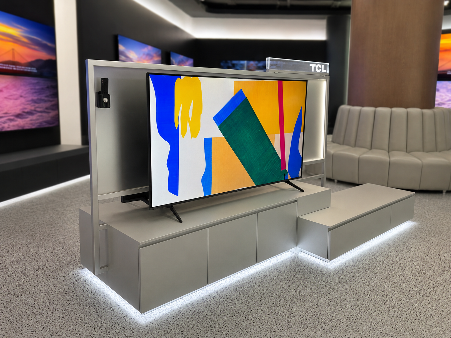 Angled showroom view of TCL double-sided television display system with central frame, television, grey cabinets, illuminated base and integrated technical communication