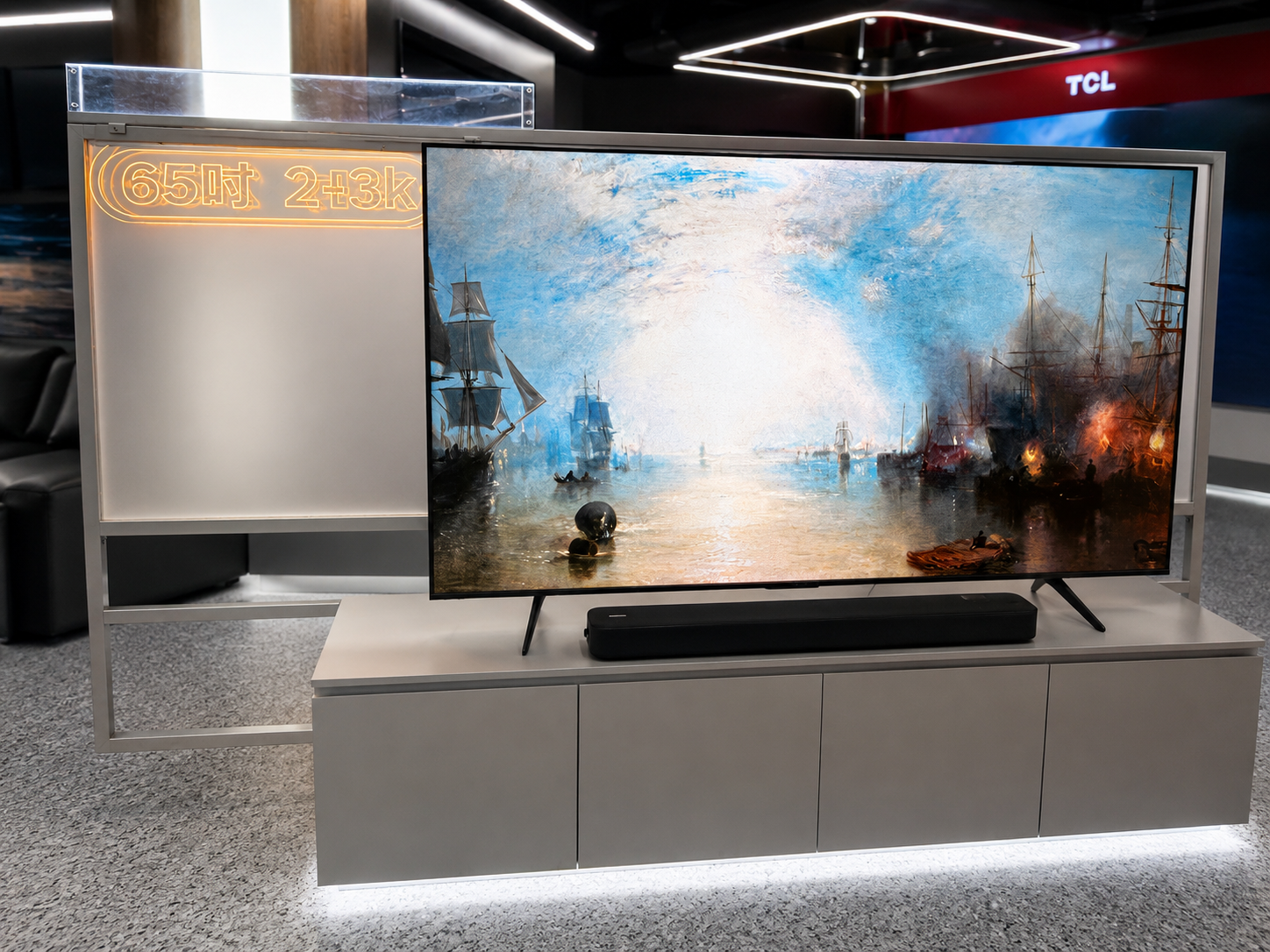 Front detail of TCL TV display with illuminated screen-size specification panel, television, soundbar and grey storage cabinets